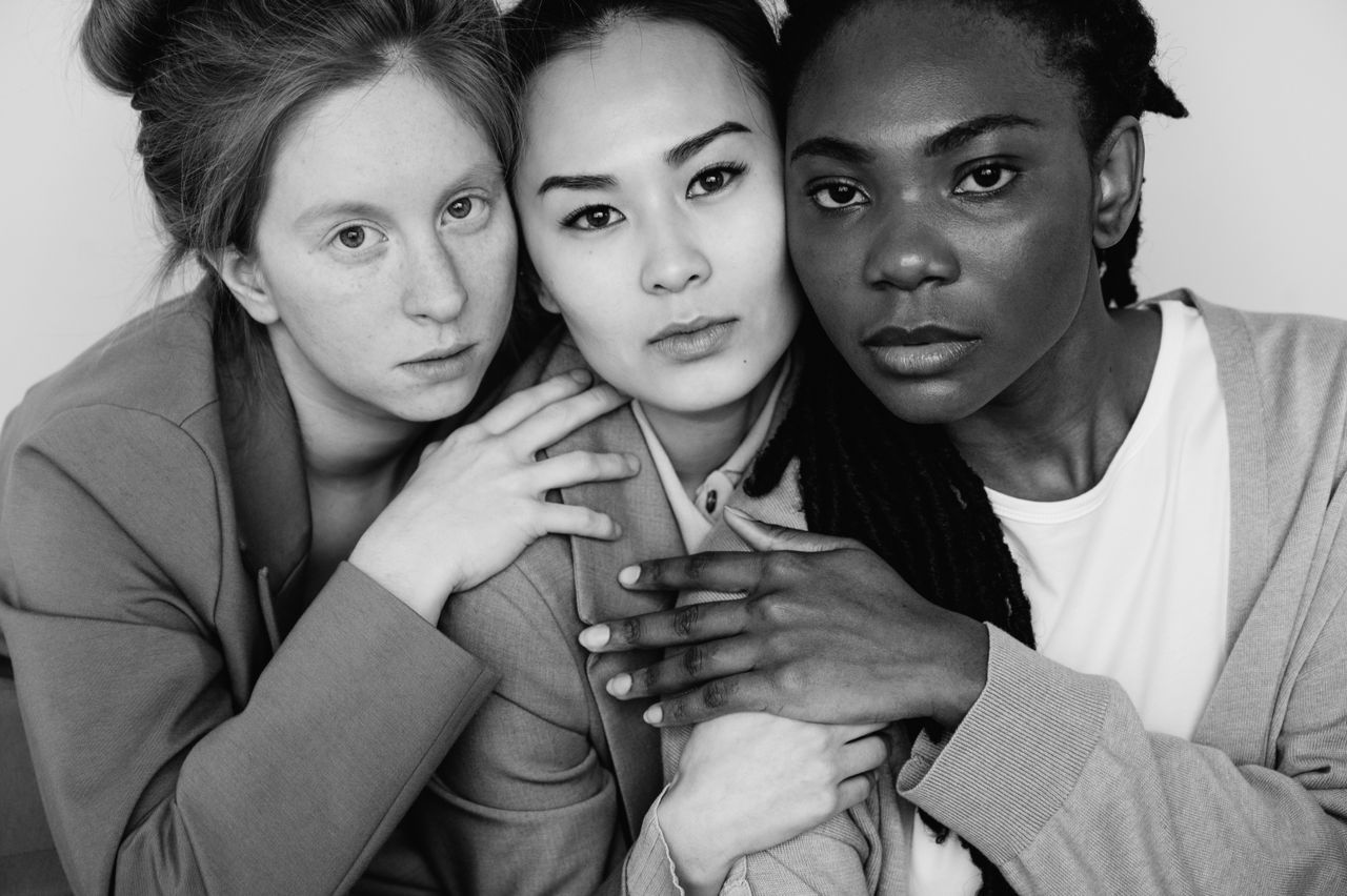 A powerful black and white portrait of three diverse women embracing with confidence.